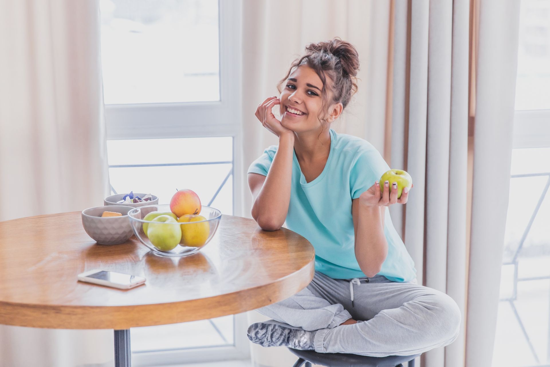 Young Happy Woman Refreshing with Cup of Coffee, Snacks and Fresh Fruit at the Kitchen Table in the Early Morning.